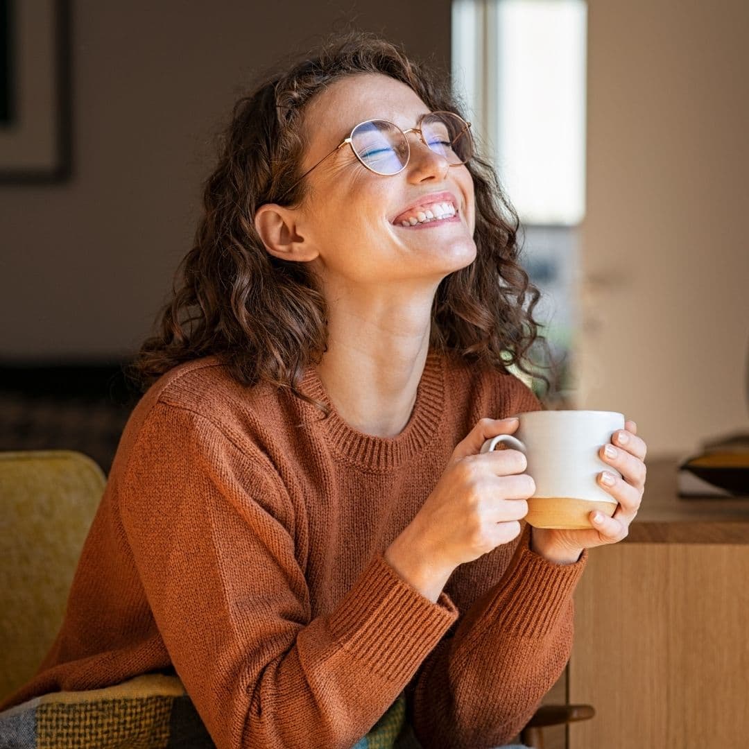A young woman smiling with a warm drink, a quiet moment of comfort at home